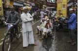 Street scene from Mumbai. To the left, a man on his bike and in the centre, several men looking directly into the camera.