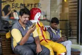 Two men on a bench with statue of Ronald McDonald